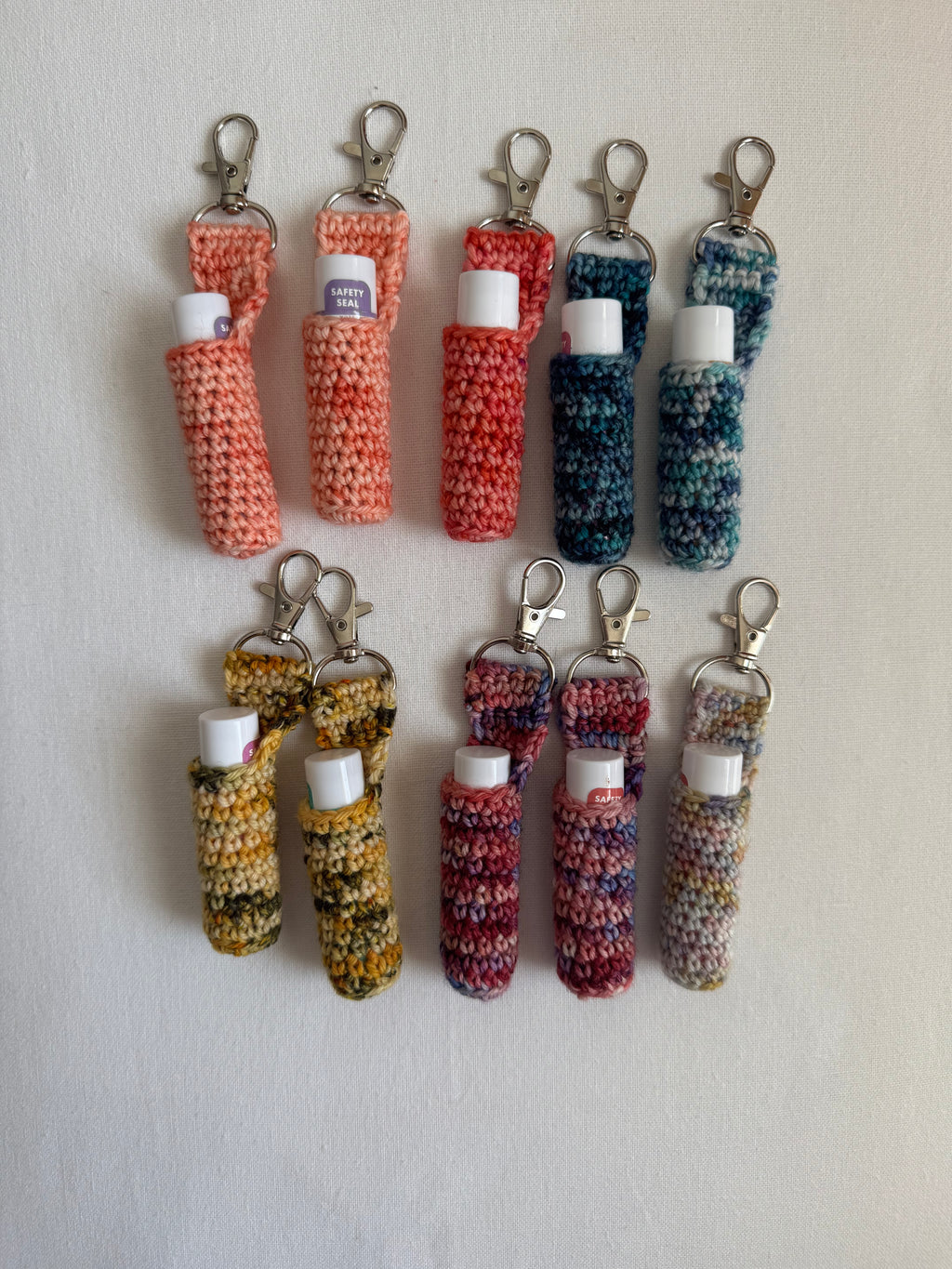 A collection of crocheted lip balm holders in various colors, each with a clip attached to the top.