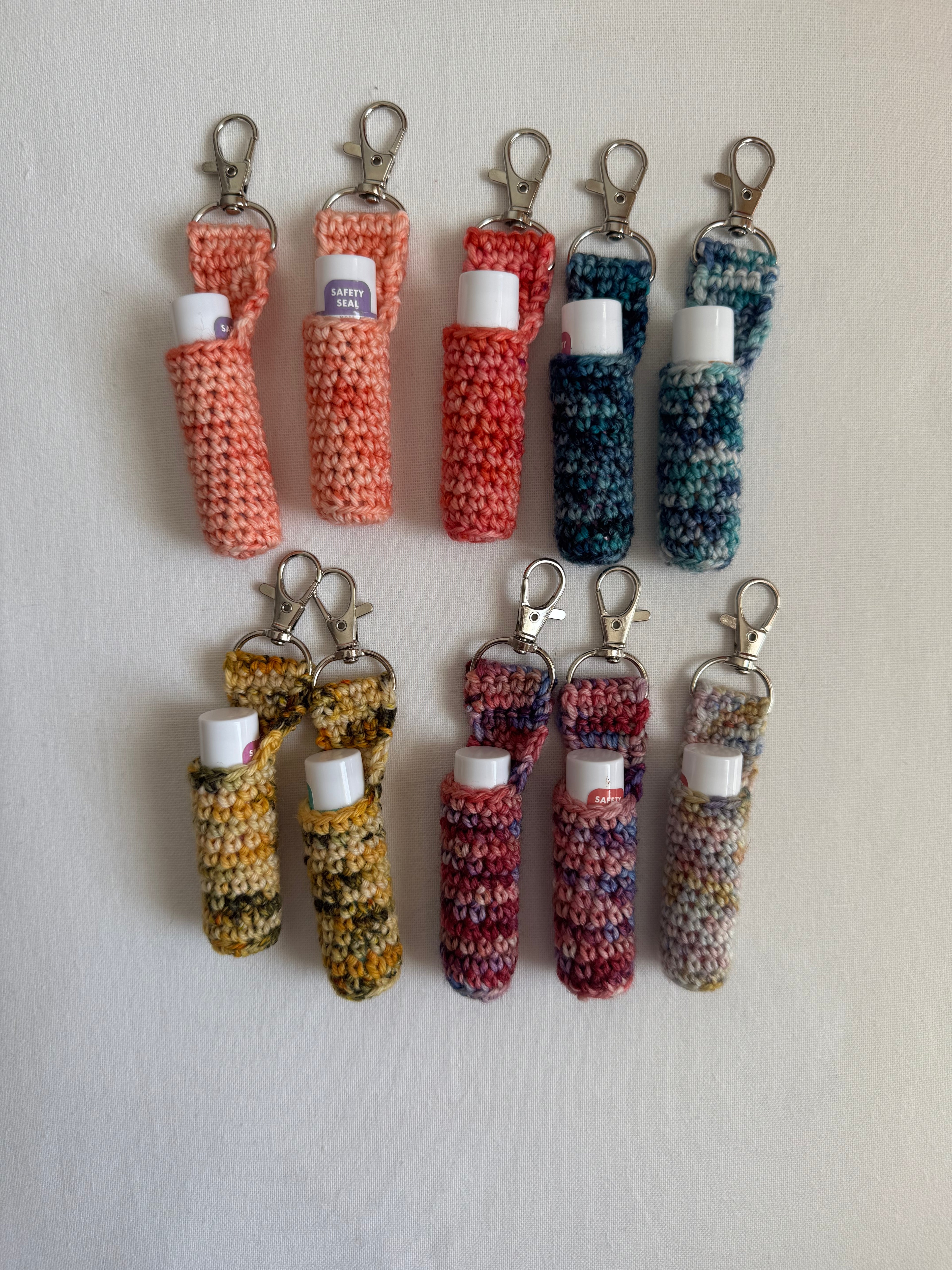 A collection of crocheted lip balm holders in various colors, each with a clip attached to the top.